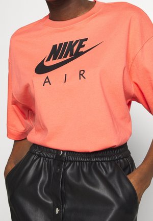 Osoba nosząca koralowy t-shirt Nike Air włożony w czarną skórzaną spódnicę z wysokim stanem, z rękami w kieszeniach.