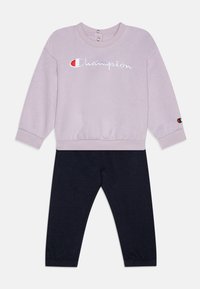 Sudadera lila con bordado de "Champion" y botones en el cuello, combinada con leggings navy. Tejido suave, puños y cintura acanalados.