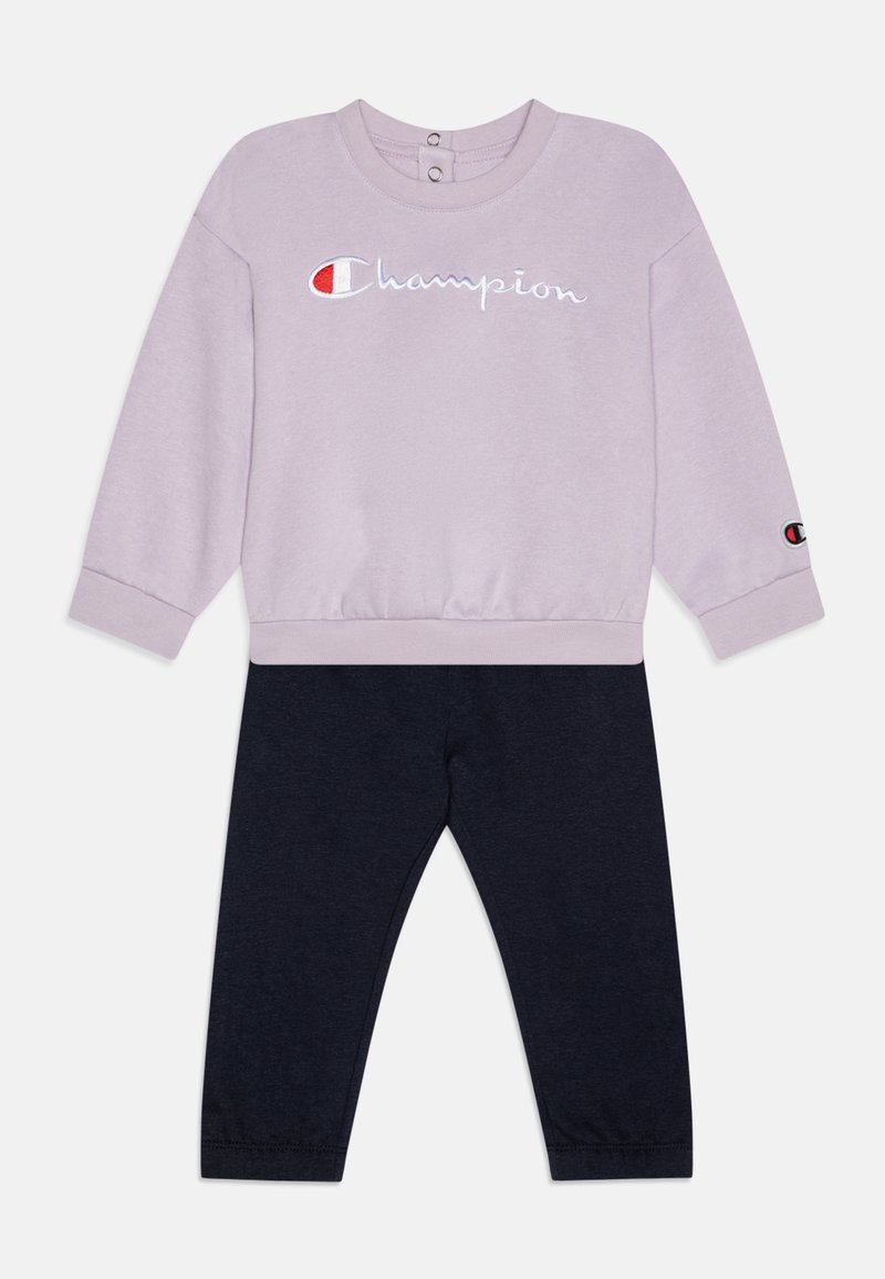 Sudadera lila con bordado de "Champion" y botones en el cuello, combinada con leggings navy. Tejido suave, puños y cintura acanalados.