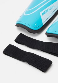 Blue shin guards with a glossy finish and white stripes, accompanied by two textured black elastic straps for secure fastening.