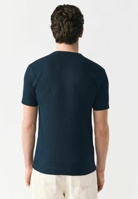Marineblauw T-shirt met korte mouwen van een textuurstof. Heeft een ronde hals en een getailleerd ontwerp, getoond vanuit de achterkant.