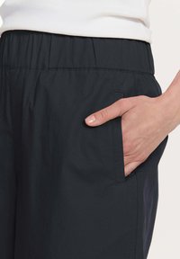 Czarne, lekkie spodnie z elastycznym pasem i kieszenią boczną. Gładka tekstura i casualowy design odpowiedni na różne okazje.