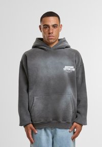 Szary, oversize'owy hoodie wykonany z miękkiej bawełnianej mieszanki, z kieszenią typu kangur i białym logo na lewej piersi.