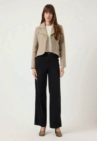 Light beige cropped jacket with gold buttons over a cream sweater, paired with high-waisted black wide-leg pants and brown heels.