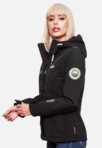 Black softshell jacket with a hood, featuring front pockets and a circular logo on the sleeve. The design is tailored with a sleek fit.