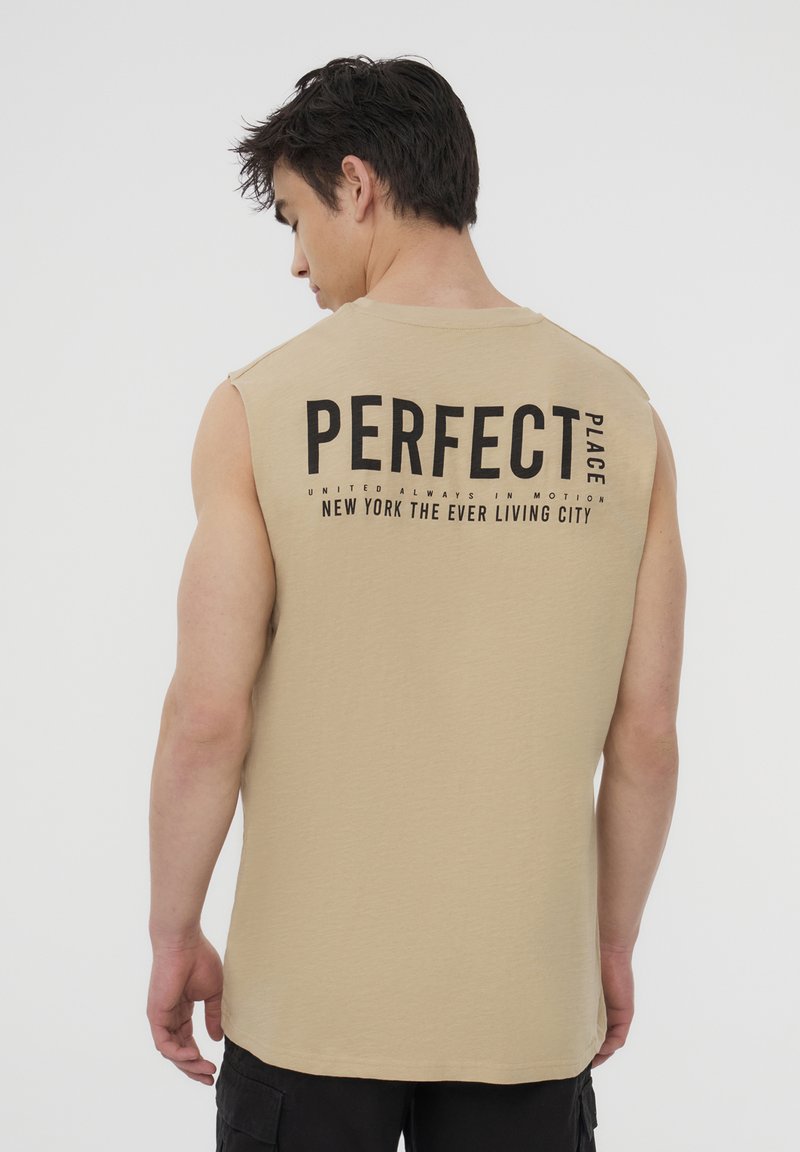 Canottiera beige senza maniche con testo stampato nero sul retro. Il testo include "PERFECT PLACE" e il nome di una città. Tessuto in cotone morbido.