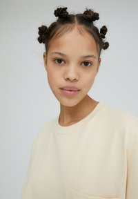 Beige oversized sweatshirt met een ronde halslijn en een klein zakje. Soepele textuur, eenvoudig ontwerp, en gedragen door een persoon met getextureerd haar.