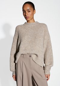 Beige ribbed knit sweater with a high neckline and drop shoulders; features a relaxed fit and subtle shine throughout the fabric.