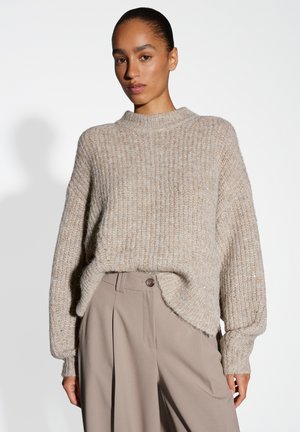 Maglione a coste beige con collo alto e spalle scese; presenta una vestibilità morbida e una leggera lucentezza su tutto il tessuto.