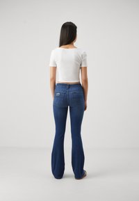 Jean bleu évasé en denim avec un lavage moyen, comportant un patch logo à l'arrière et un haut près du corps à manches courtes blanc.