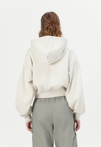 Geknipte hoodie in lichtbeige, gemaakt van zachte stof, met een capuchon en pofmouwen. Gepaard met olijfgroene cargo pants.