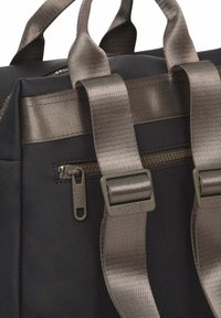 Bolsa tote negra con tejido resistente, cremalleras metálicas y correas anchas y brillantes de color marrón. Presenta un logotipo prominente en la hebilla de la correa.