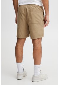 Khaki shorts with a textured fabric, elastic waistband, and back pocket. Paired with white socks and light-colored sneakers.