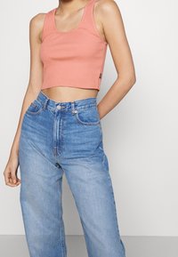 Débardeur court à côtes de couleur corail clair, associé à un jean en denim bleu clair taille haute. Présente une texture subtile et une silhouette ajustée.