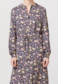 Robe fleurie en tissu violet foncé, avec une fermeture à boutons à l'avant, des manches longues, une taille cintrée, et un motif de fleurs et de feuilles colorées.