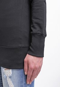 Svart langermet topp laget av glatt bomull, har rund hals og ribbestrikkede mansjetter, kombinert med revne blå denimjeans.