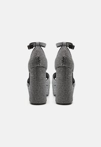 Černé platformní podpatky zdobené řadami stříbrných rhinestones, s nastavitelnými řemínky kolem kotníku a zaobleným tvarem špičky.