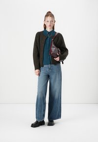 Dark green knitted cardigan over a blue collared shirt, wide-leg blue jeans, and black platform shoes, with a maroon crossbody bag.