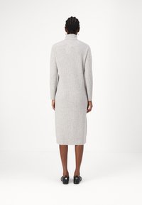 Robe en tricot gris côtelé avec un col montant, des manches longues et un ourlet jusqu'aux genoux. Associée à des chaussures noires, elle présente une texture lisse et une coupe ajustée.