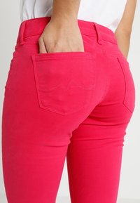 Figurbetonte rosa Jeans mit Details an der Gesäßtasche und einer glatten Textur. Verfügt über ein dezentes Nähtmuster auf der Tasche.