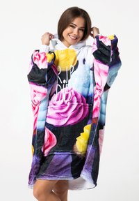 Manta con capucha de gran tamaño que presenta vibrantes patrones florales, predominantemente rosas en tonos rosa y amarillo. Hecha de un material suave y aterciopelado con un fondo blanco.