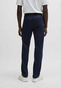 Middengrijze broek met een rechte pasvorm, voorzien van twee achterzakken en een gladde stoftextuur. G gedragen met een wit shirt en witte sneakers.