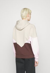 Kapuć sweatshirt s blokiranim bojama u bež, ružičastoj i smeđoj. Tekstura tkanine s trokutastim uzorkom na stražnjoj strani.