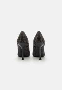 Sorte højhælede sko med spids t�å, prydet med metalliske nitter. Glat tekstur med en blank hæl, der skaber et moderne design.