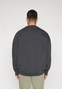 Sweatshirt oversized cinza escuro com gola redonda, punhos e bainha canelados. Feito de tecido texturizado. Vista traseira apenas.