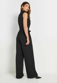 Svart jumpsuit med ärmlös design, krage, cinchad midja och vida byxor. Slät tyg med rena linjer och enkla detaljer.