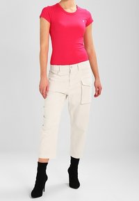 Tight rosa kortärmad topp i kombination med krämfärgade cargobyxor med sidofickor, kompletterad av svarta ankelstövlar.