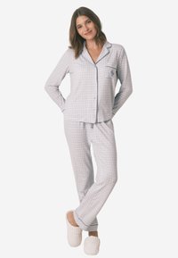 Bawełniany zestaw piżamowy w jasnoniebieską kratkę, składający się z koszuli zapinanej na guziki z kieszonką oraz pasujących spodni, noszony z białymi kapciami.