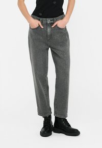 Jeans in denim grigio con una vestibilità ampia, gamba diritta, vita alta, caratterizzati da tasche frontali e una leggera texture marmorizzata, abbinati a stivali militari neri.