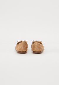 Brown woven ballet flats with a soft texture, featuring a minimalistic design, bow detail on the back, and a rounded toe.