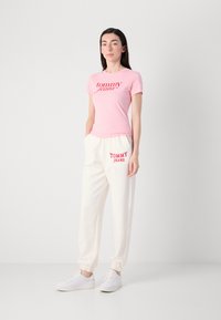 Roze katoenen T-shirt met "tommy jeans" logo, gecombineerd met witte fleece joggingsbroek met "TOMMY JEANS" tekst en witte sneakers.