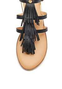 Sandal de cuero negro con múltiples correas horizontales y un detalle decorativo de flecos. Suela de color marrón claro con textura suave.