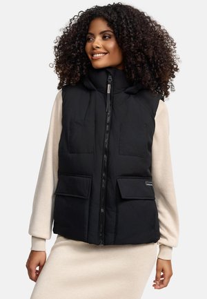 Black padded vest with a hood, featuring a central zipper and two front patch pockets. Worn over a beige long-sleeve top.