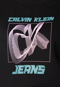 Černé tričko s grafickým designem, kde jsou slova "CALVIN KLEIN" v tyrkysové barvě a "JEANS" v světle modré, obtažené bílými a růžovými liniemi.