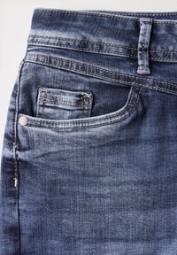 Jeans de denim en un tono azul oscuro con un ligero desvanecimiento. Presentan un diseño clásico de cinco bolsillos, con un pequeño bolsillo para monedas y herrajes plateados.