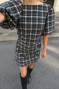 Robe à carreaux noir et blanc avec des manches bouffantes, texture froncée, décolleté carré et courte longueur, associée à des bottes noires montantes.