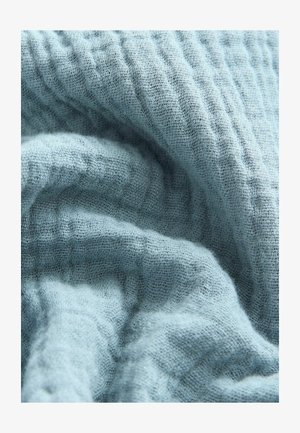 Vaaleansininen teksturoitu kangas aaltoilevalla kuviolla. Pehmeä, hieman rypistynyt pinta, joka näyttää hengittävältä ja viittaa kevyisiin materiaaleihin.