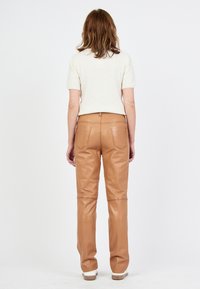 Tan leren broek met een strakke pasvorm, voorzien van achterzakken en een gladde textuur. De outfit bestaat uit een lichtgebreide trui met korte mouwen.