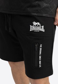 Sorte cargoshorts med en lynlås-lomme, prydet med et hvidt Lonsdale London-logo og tekst. Fremstillet af glat, slidstærkt stof.