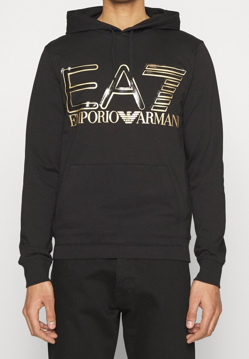 Svart hoodie i mjukt tyg med en glänsande gul och silver logotyp "EA7 Emporio Armani" över bröstet. Framlomma med ficka.