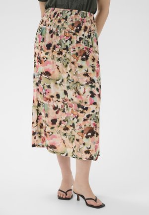 Femme portant une jupe florale mi-longue avec une taille smockée et des sandales à talons noires sur un fond uni.