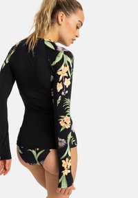 Rash guard noir à manches longues avec des motifs floraux colorés sur les manches, associé à un bas de bikini assorti. Matière lisse et extensible.