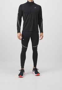 Czarny sportowy top z długim rękawem i półzamkiem, w połączeniu z czarnymi legginsami z odblaskowymi akcentami. Uzupełniony czarno-czerwonymi butami sportowymi.