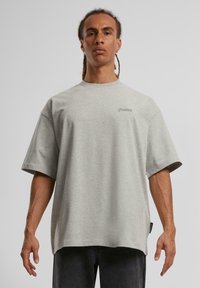 Sivý oversized tričko vyrobené z bavlneného zmesi. Má krátke rukávy, okrúhly výstrih a jemne vyšívané logo na hrudi.