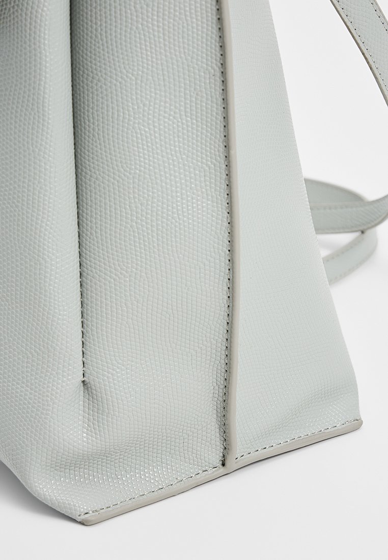 Gros plan d'un coin de sac à main en cuir texturé gris clair avec des coutures visibles et une forme structurée.