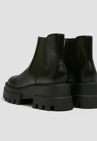 Bottes Chelsea en cuir noir avec semelles basses épaisses et panneaux latéraux élastiques. Caractérisées par une texture lisse et une construction robuste.